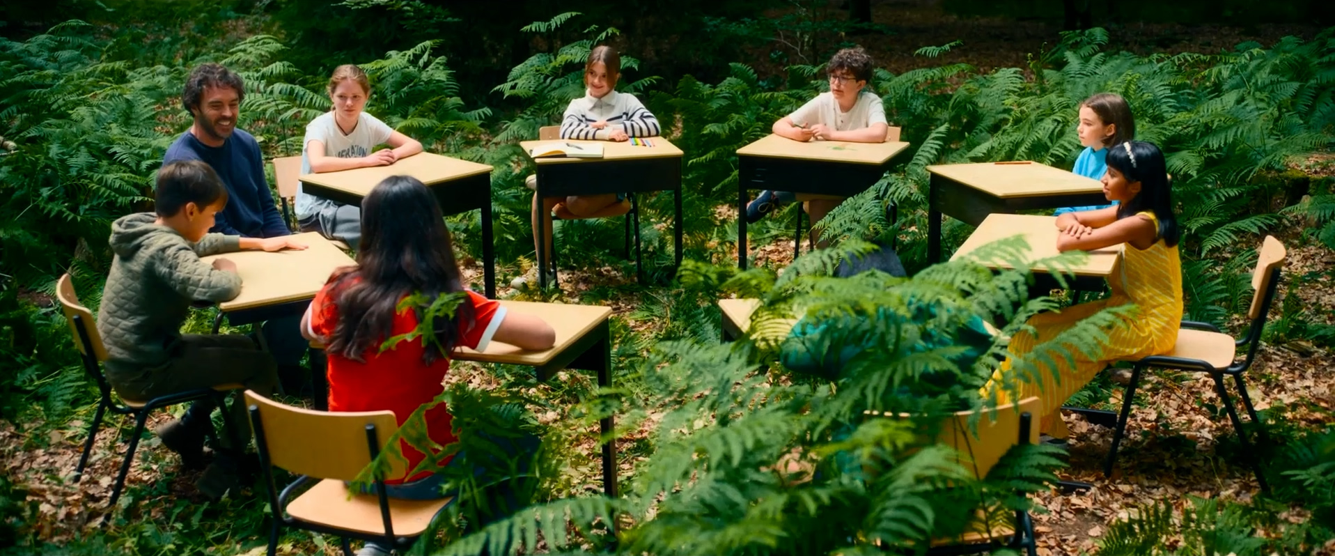Die acht Kinder aus dem Film sitzen mit dem Regisseur Damon Gameau an Schulpulten in einem Kreis mitten im Wald.