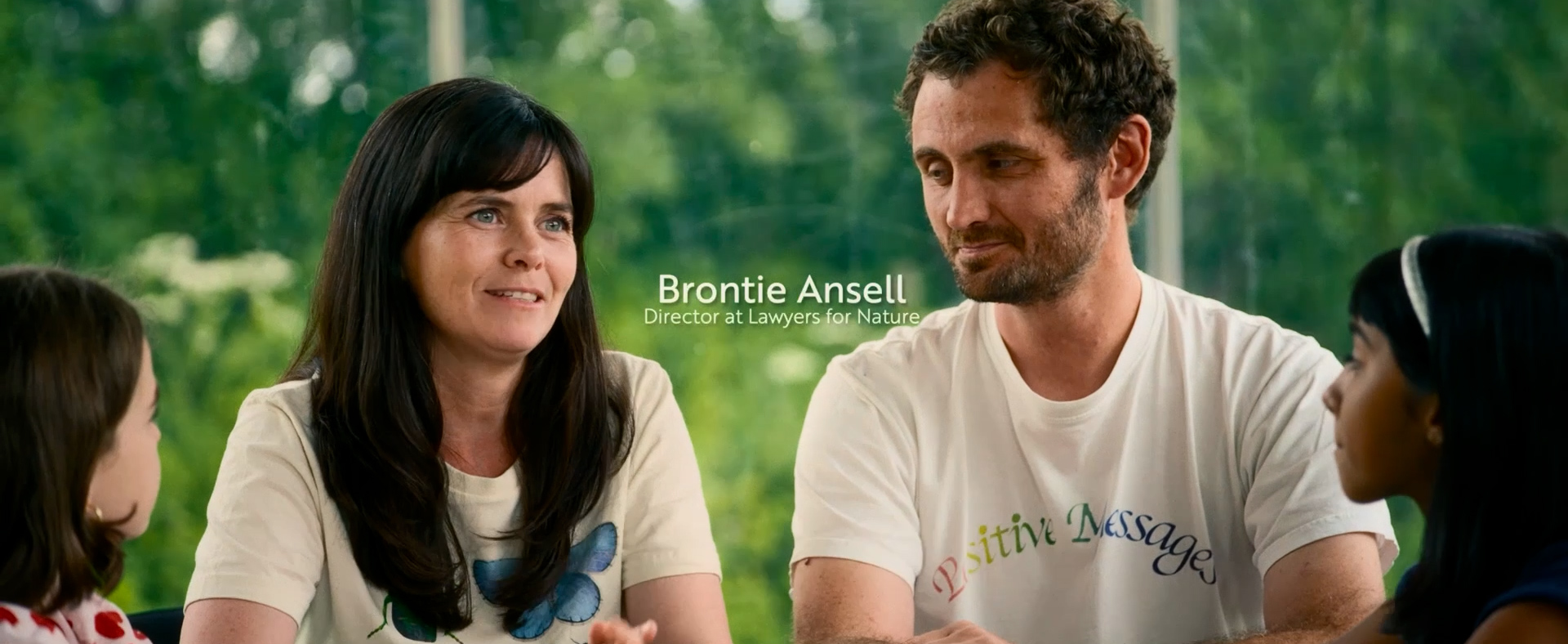 In der Mitte sitzen eine dunkelhaarige Frau und ein Mann im weißen T-Shirt nebeneinander. Links und rechts von ihnen sind jeweils die Profile zwei der Kinder aus dem Film im Anschnitt zu sehen. Neben der Frau ist der Schriftzug „Brontie Ansell – Director at Lawyers for Nature“ eingeblendet.