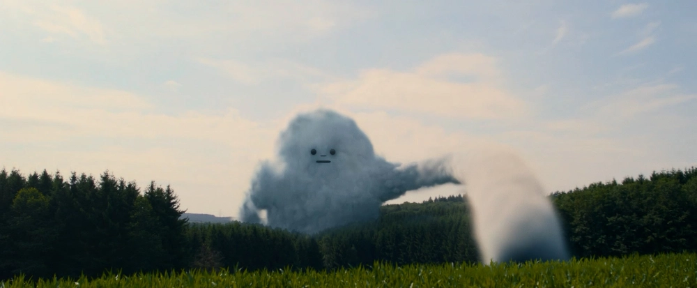 Eine Figur in Form einer großen Wolke mit Gesicht saugt mit einem Arm aus Wolken an einer Wiese.