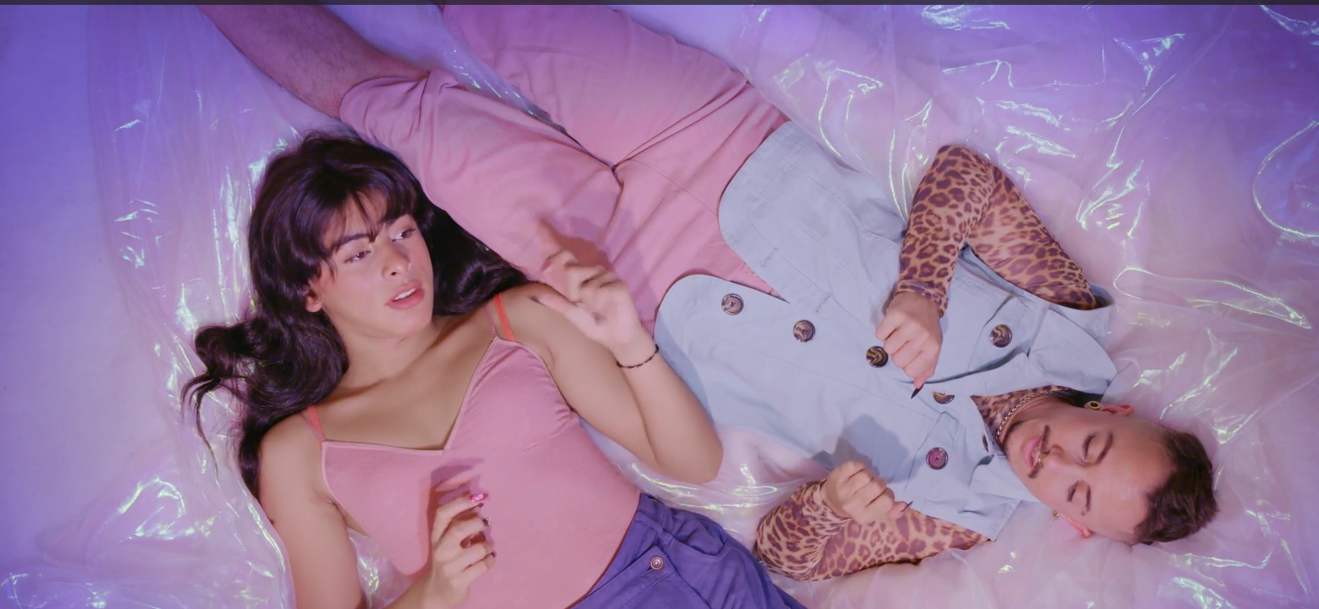 Karla und Kani liegen auf einer rosa schimmernden Plastikfolie. Die Aufnahme aus der Vogelperspektive zeigt ihre farblich abgestimmten Outfits in rosa und hellblau und ihre lackierten Fingernägel.