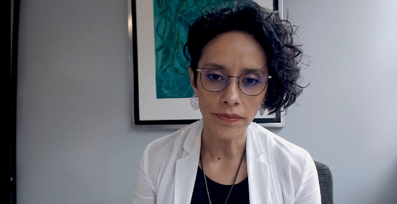 Nahaufnahme der Schulberaterin auf einem Bürostuhl. Sie blickt ernst in die Kamera und trägt eine weiße Bluse, Brille und Ohrringe.